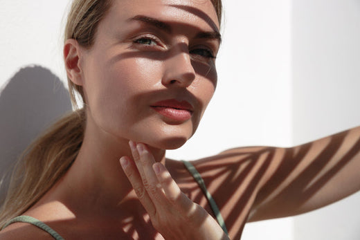 A woman in partial shadow touching her cheek — symbolizing the care, confidence, and nuance involved in acne scar prevention and treatment.
