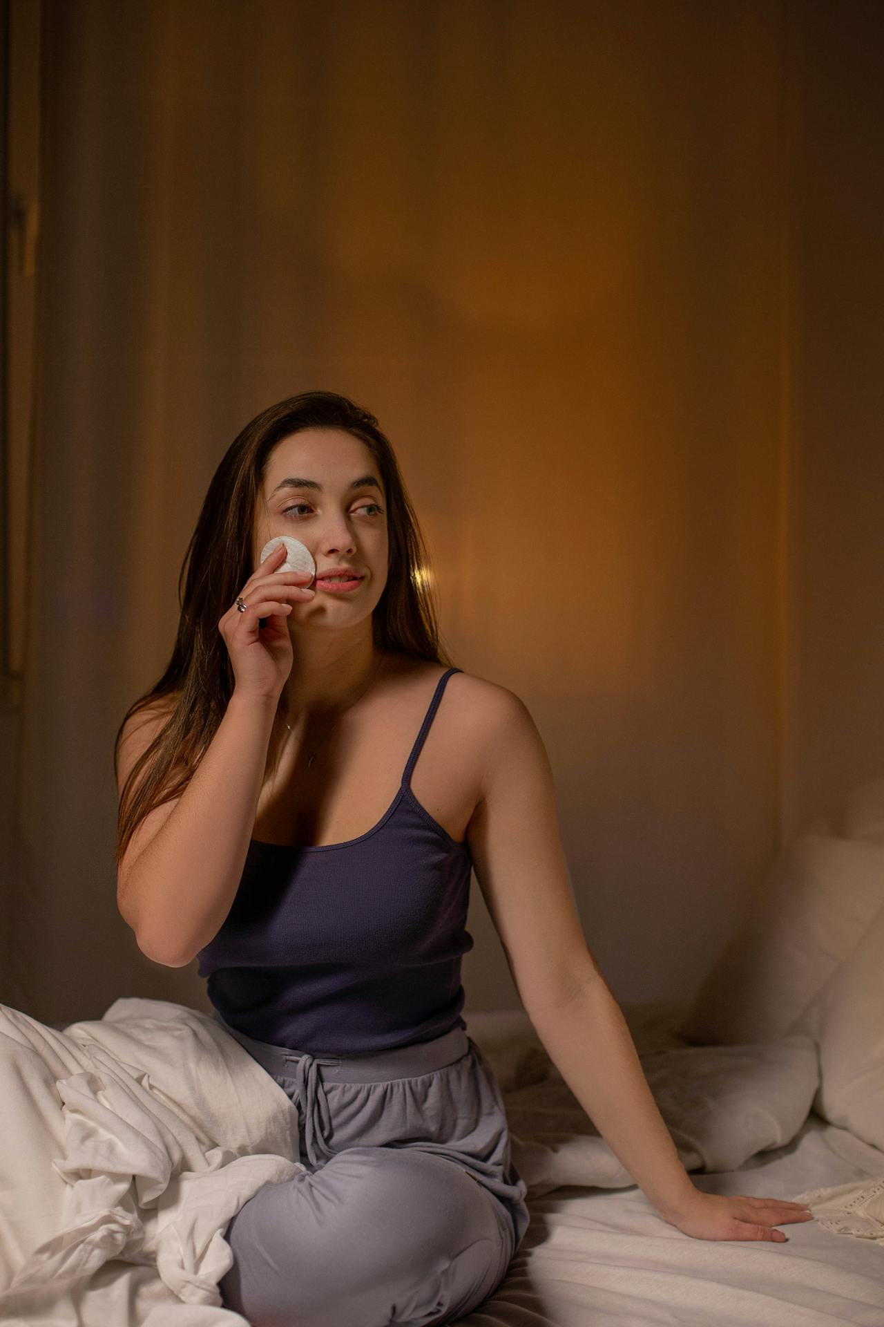 Woman doing her nighttime skincare routine in bed with an Exoceuticals® product — part of a beauty sleep feature.