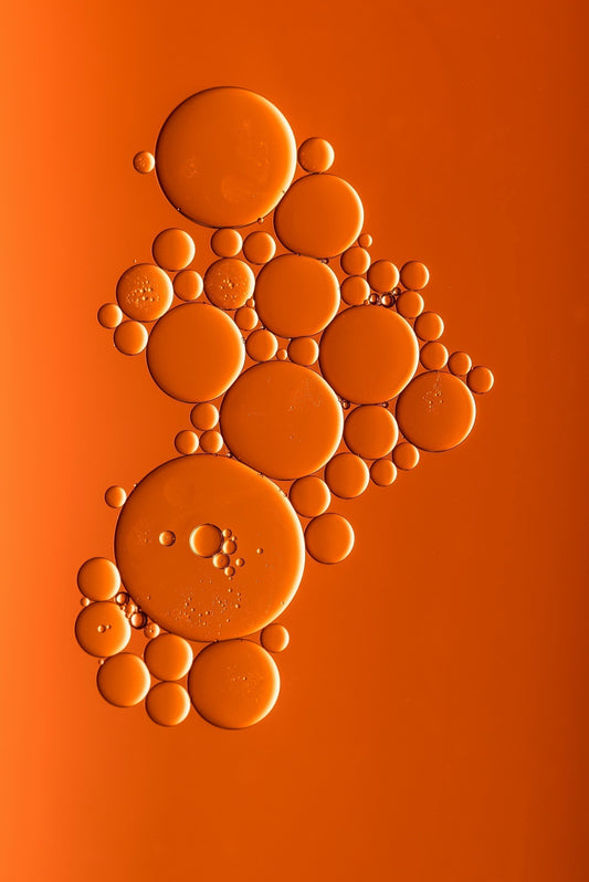 An abstract cellular motif of oil droplets on vibrant orange — symbolizing Exoceuticals®’ advanced exosome technology and the science of targeted skin communication.